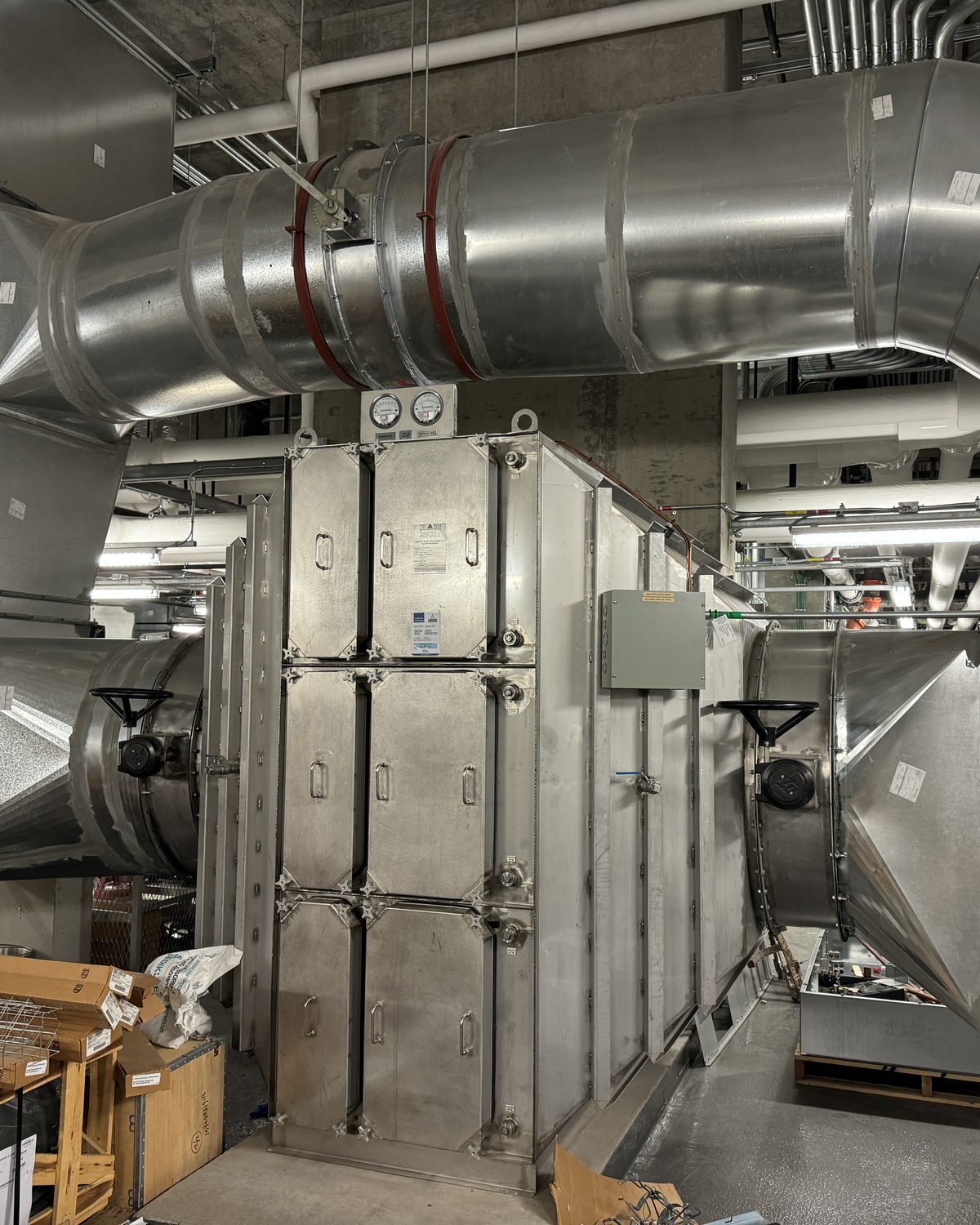 Large stainless steel isolation room HEPA exhaust housing with spiral ductwork in a hospital mechanical room